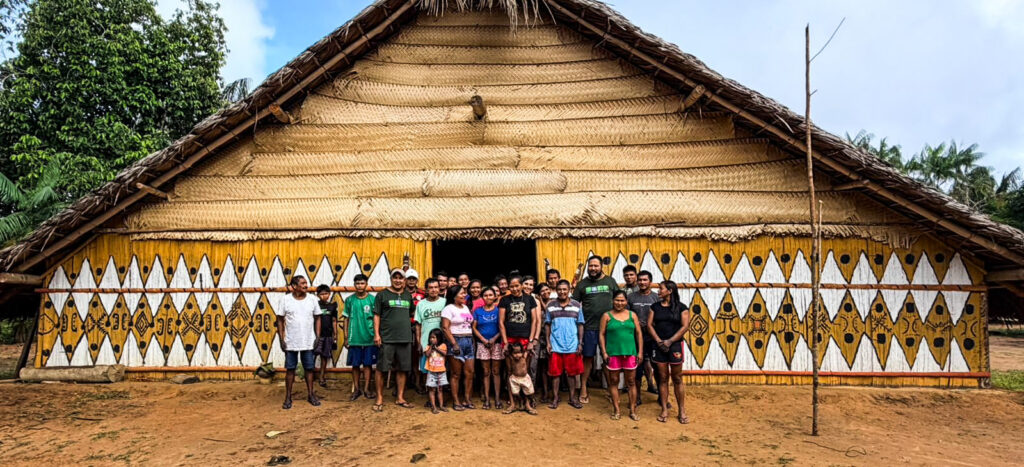 Comunidade indígena reunida em frente à maloca