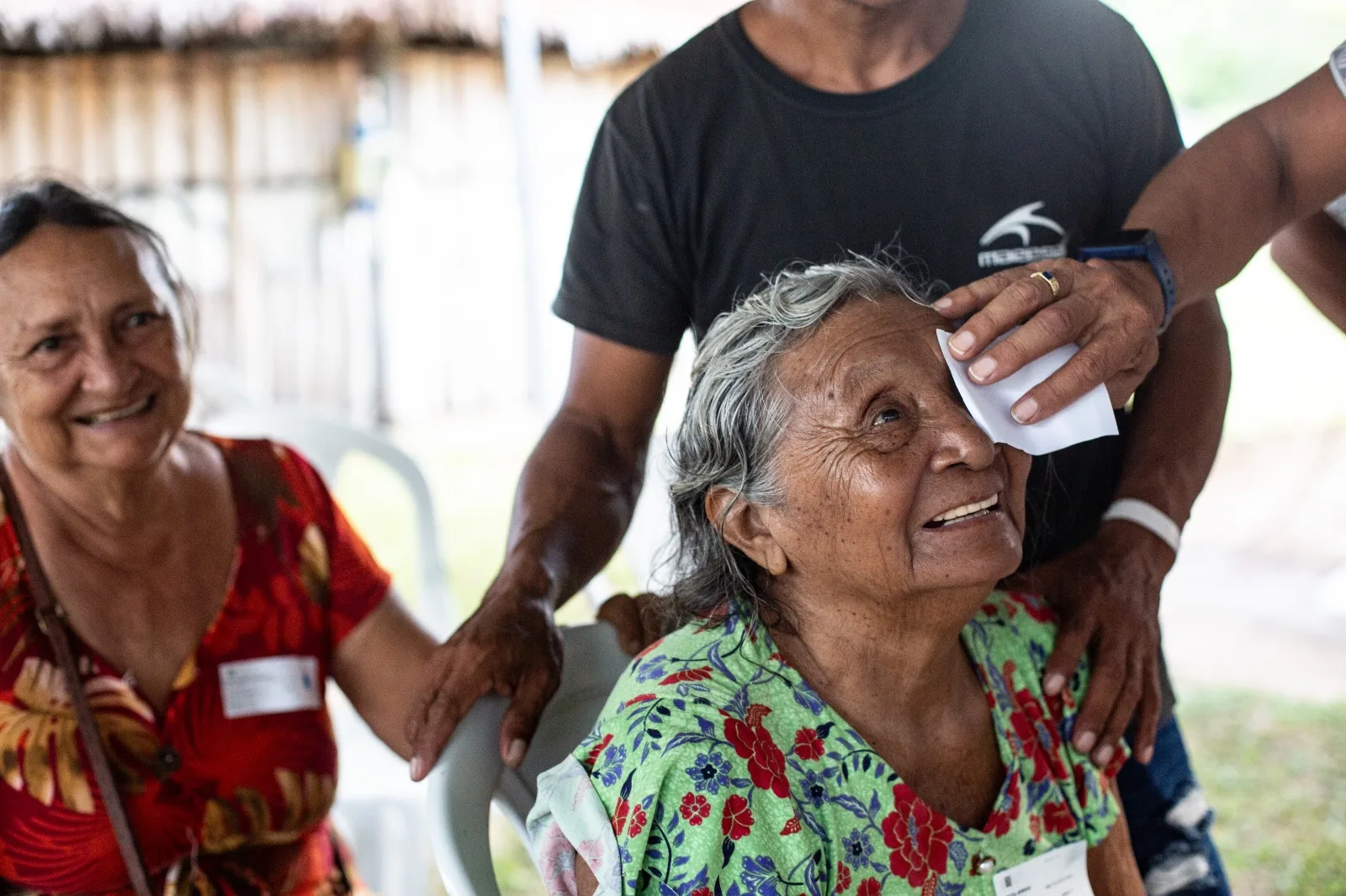 Paciente idosa sorri amparada por voluntárias depois do atendimento